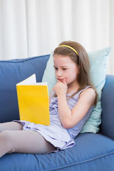 Kleines Mädchen liest auf Couch — Stockfoto