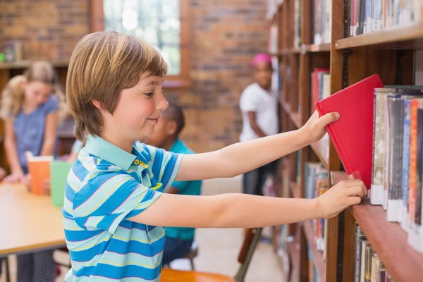 Roztomilý žák hledá knihy v knihovně — Stock fotografie