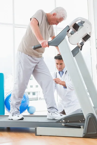 Senior man on treadmill with therapist crouching — Stock Photo, Image