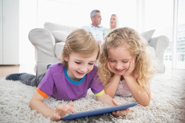 Hermanos usando tableta digital en alfombra en casa —  Fotos de Stock