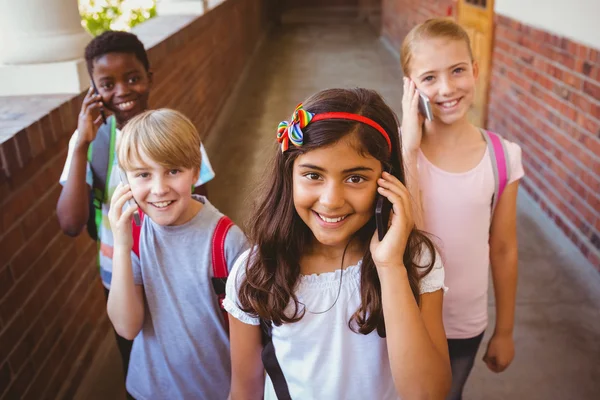 Écoliers utilisant des téléphones cellulaires dans le couloir scolaire — Photo