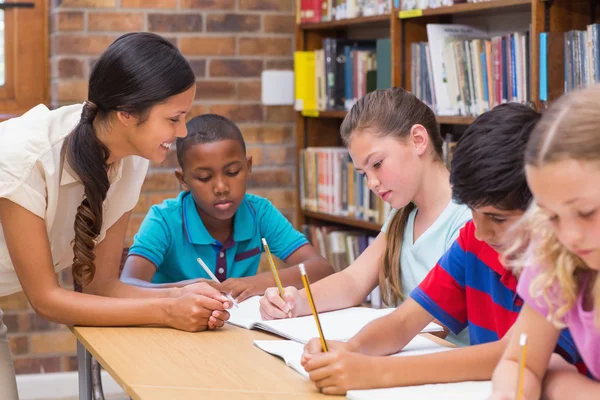 Mooie leraar helpt leerlingen in bibliotheek — Stockfoto