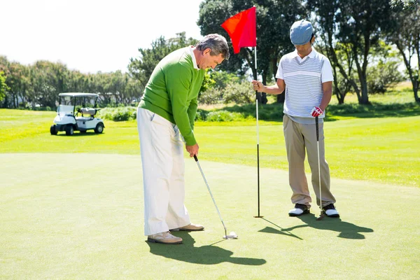 Golfer holding hole flag for friend putting ball — Stock Photo, Image