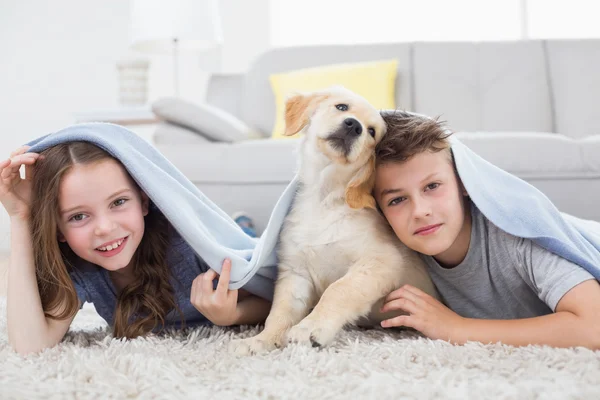 Симпатичные братья и сестры с собакой под одеялом в гостиной — стоковое фото