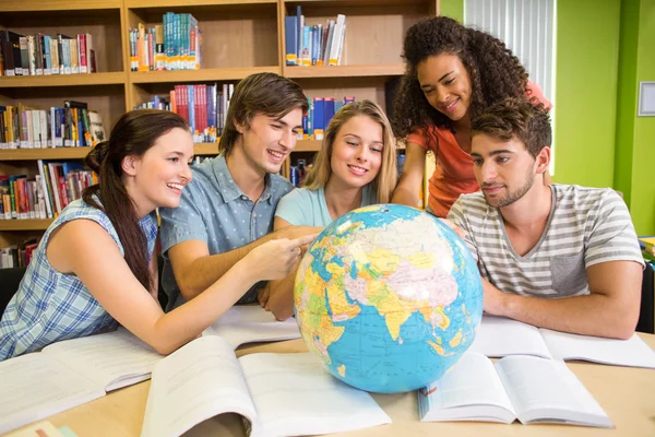 Estudantes universitários apontando para globo na biblioteca — Fotografia de Stock