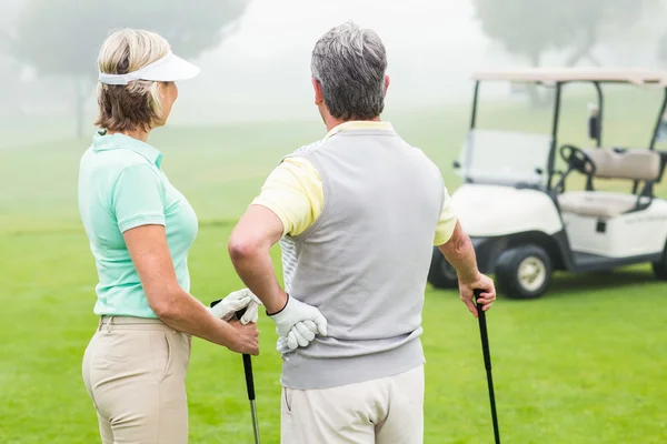 Happy golfing couple with golf buggy behind — Stock Photo, Image