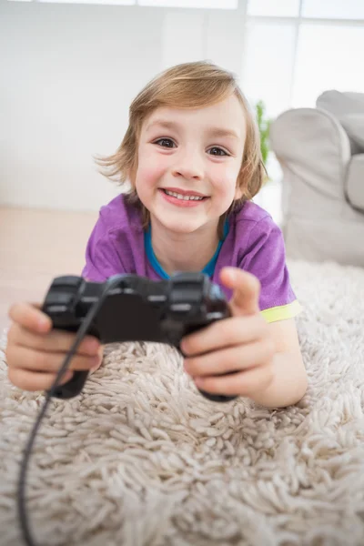 Glücklicher Junge spielt Videospiel, während er auf Teppich liegt — Stockfoto