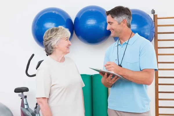 Trainerin schreibt mit Seniorin auf Klemmbrett — Stockfoto