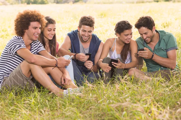 Amigos felices en el parque usando sus teléfonos —  Fotos de Stock