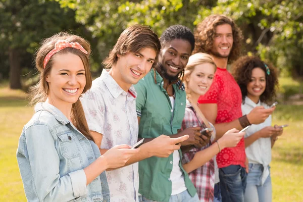 Amigos felizes no parque usando seus telefones — Fotografia de Stock