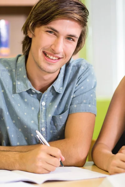 Feliz estudiante masculino haciendo deberes en la biblioteca — Foto de Stock