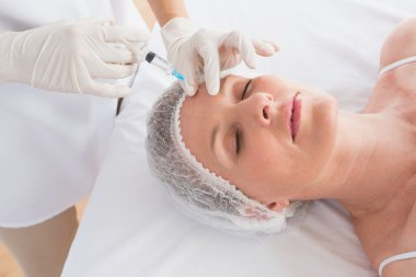 Woman receiving botox injection on forehead clipart