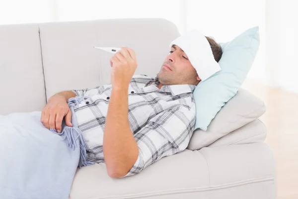 Hombre enfermo comprobando la temperatura en el termómetro — Foto de Stock