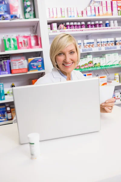 Farmacista sorridente usando il computer portatile e tenendo la prescrizione — Foto Stock