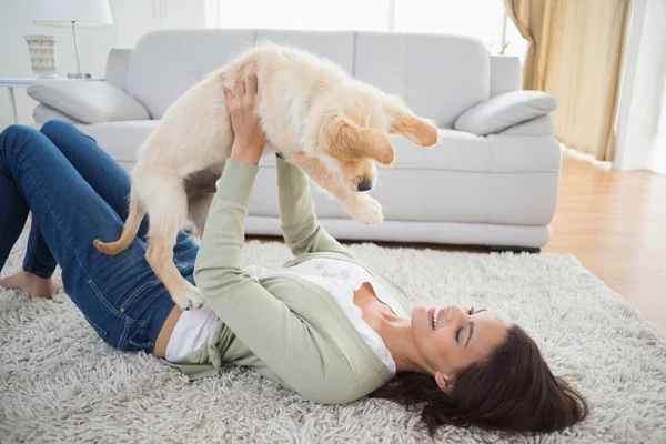 Mulher levantando filhote de cachorro enquanto deitado — Fotografia de Stock