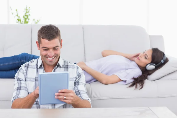 Hombre usando tableta PC mientras que la mujer escucha música en los auriculares — Foto de Stock