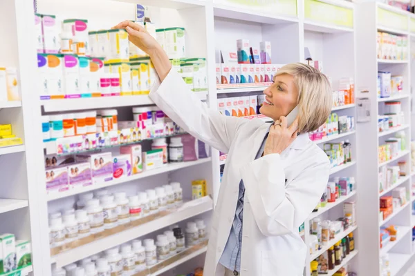 Lächelnder Apotheker telefoniert und nimmt Medikamente aus dem Regal — Stockfoto