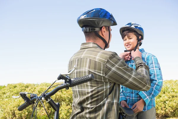 Отец прикрепляет к сыну велосипедный шлем — стоковое фото