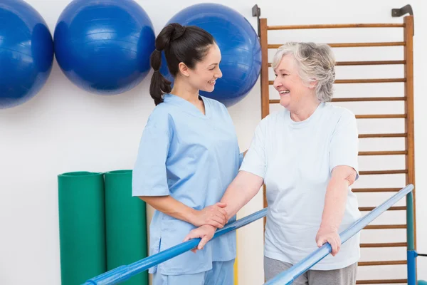Senior vrouw lopen met parallelle staven met therapeut — Stockfoto