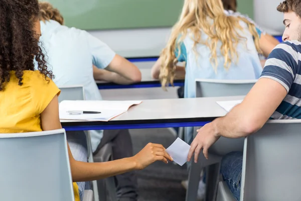 Estudante feminina passando nota para amigo em sala de aula — Fotografia de Stock