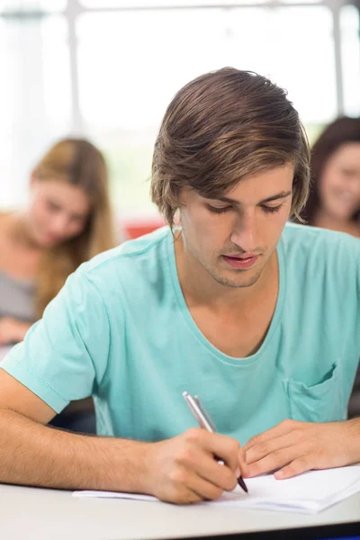 Männlicher Schüler schreibt Notizen im Klassenzimmer — Stockfoto