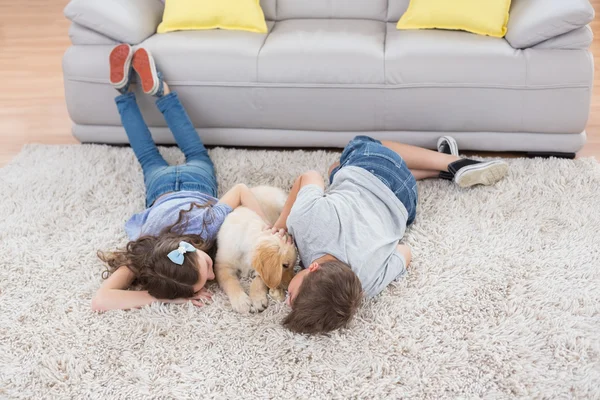 Geschwister mit Hund auf Teppich liegend — Stockfoto