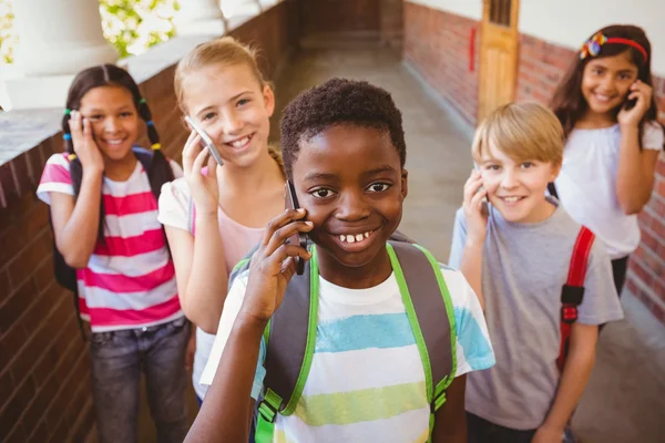 Schoolkinderen met behulp van mobiele telefoons in school corridor — Stockfoto