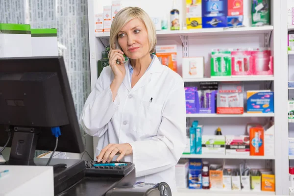 Farmacêutico loiro usando computador enquanto telefona — Fotografia de Stock