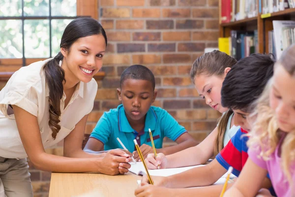 Pretty teacher helping pupils in library — Stock Photo, Image