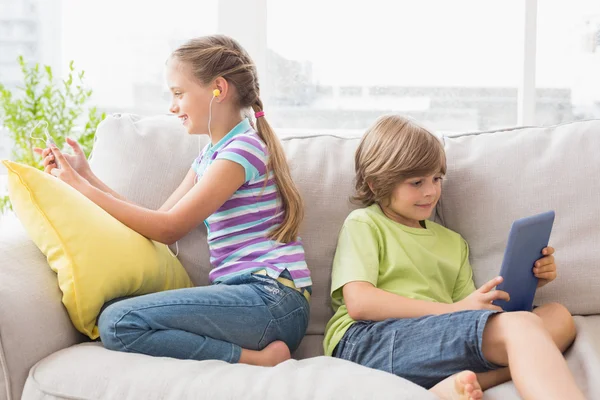 Siblings using technologies on sofa — Stock Photo, Image