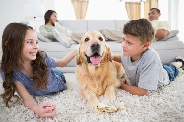 Geschwister streicheln Hund auf Teppich — Stockfoto