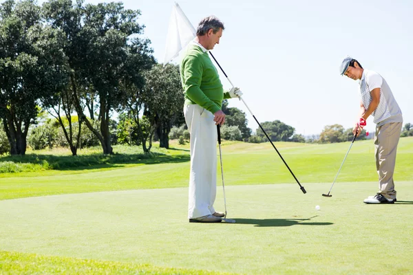 Golfista in possesso di foro bandiera per amico mettendo palla — Foto Stock