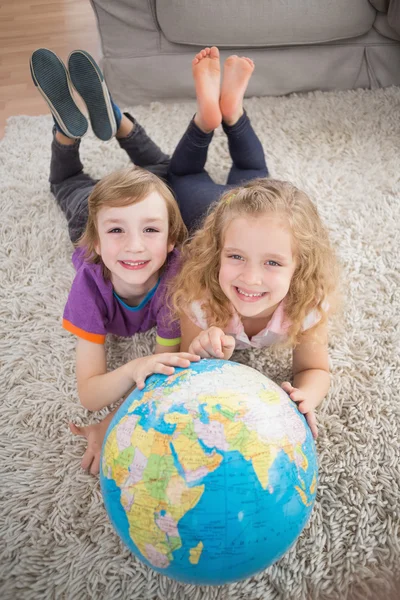 Брат и сестра с глобусом лежат на ковре — стоковое фото