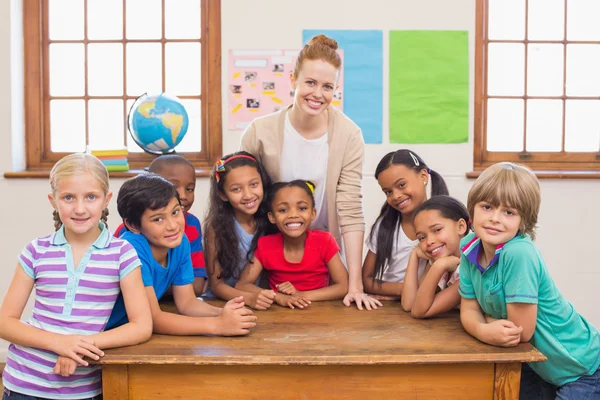 Cute pupils and teacher smiling at camera in classroom — Stock Photo, Image