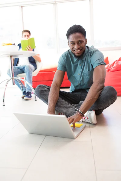 Mosolygó fiatal ember használ laptop emeleten — Stock Fotó