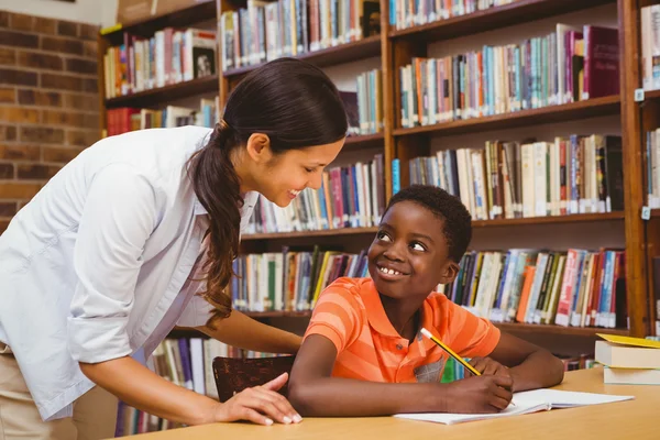 Teacher assisting boy with homework in library — Stock Photo, Image