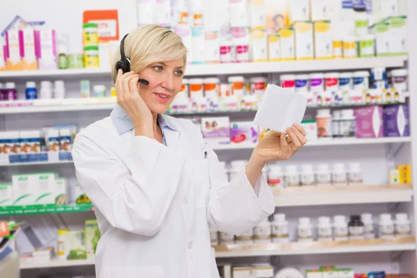 Farmacêutico com fone de ouvido lendo uma prescrição — Fotografia de Stock