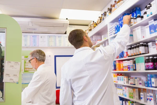 Farmacêutico de jaleco retirando frasco da prateleira — Fotografia de Stock