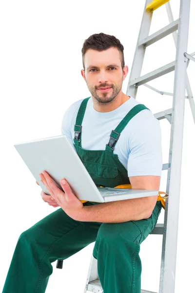 Carpenter sitting on ladder using laptop — Stock Photo, Image