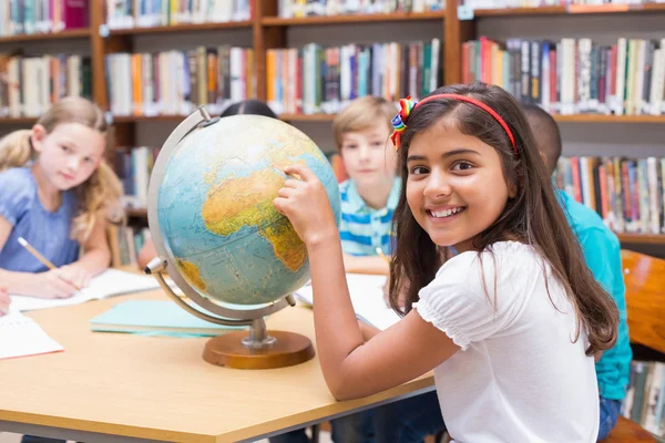 Niedliche Schüler schauen in Bibliothek auf Globus — Stockfoto