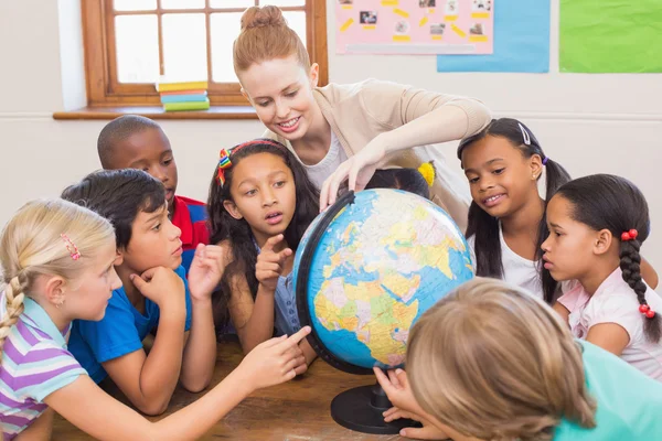 Симпатичные ученики и учитель в классе с глобусом — стоковое фото