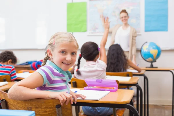 Graziosa pupilla sorridente a camera a suo scrivania in classe — Foto Stock