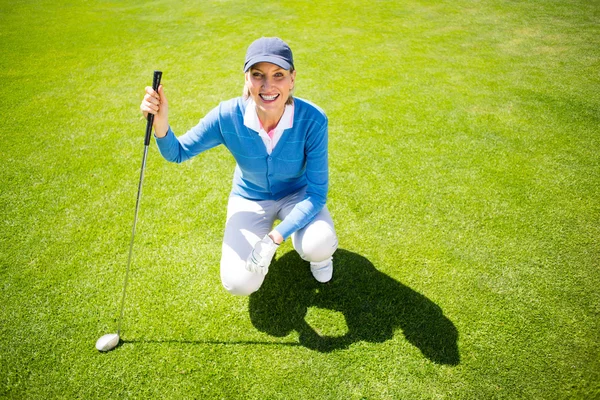 Улыбающаяся женщина-гольфист, стоящая на коленях на зеленом — стоковое фото