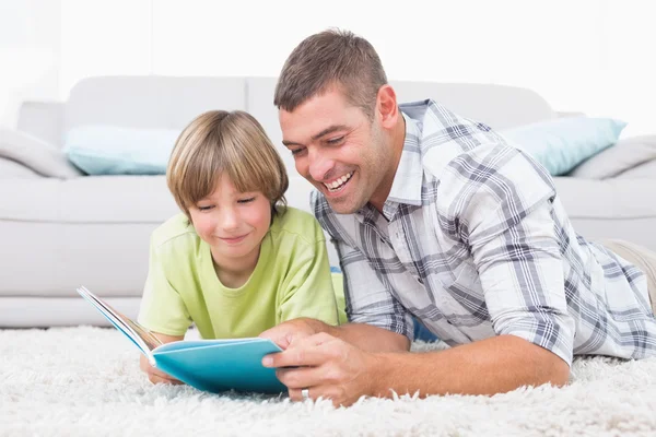 Father and son reading book while lying on floor — Stock Photo, Image