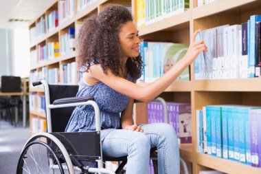 Smiling disabled student in library picking book clipart