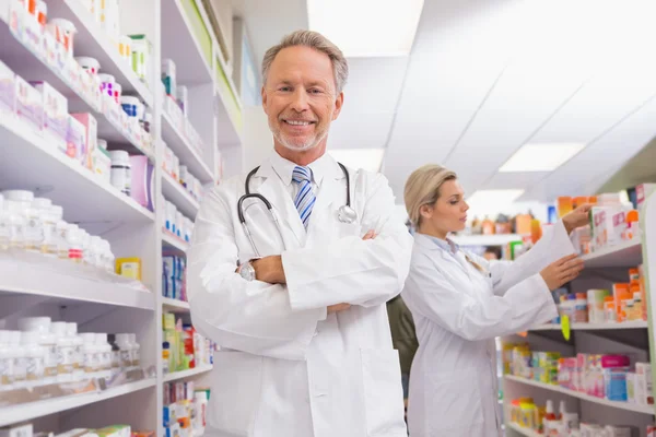 Pharmacist with arms crossed and trainee behind — Stock Photo, Image