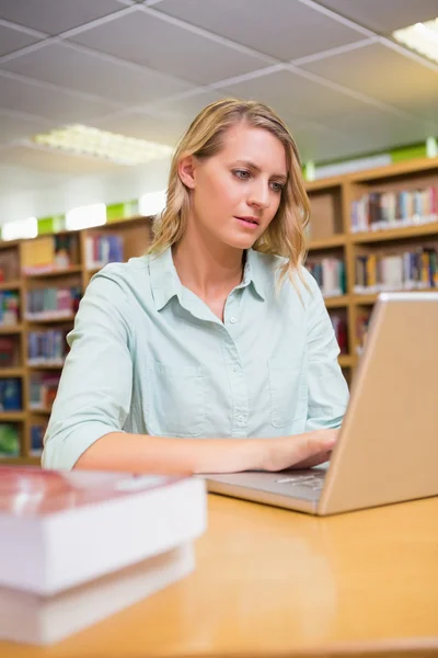 Estudante bonito estudando na biblioteca com laptop — Fotografia de Stock