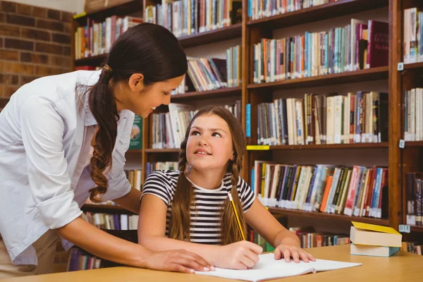 Lärare hjälpa flickan med läxläsning i biblioteket — Stockfoto