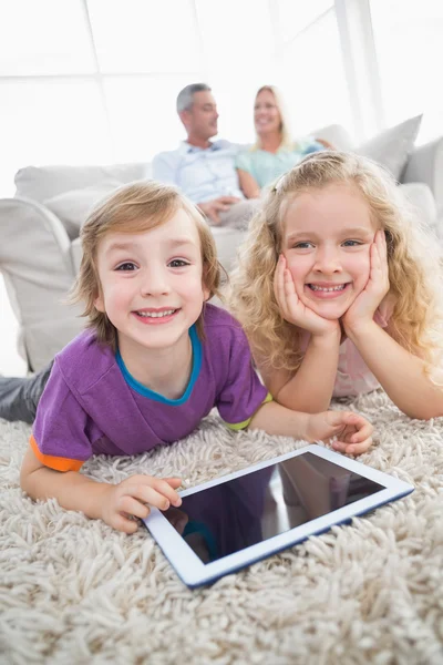 Geschwister mit digitalem Tablet liegen auf Teppich — Stockfoto