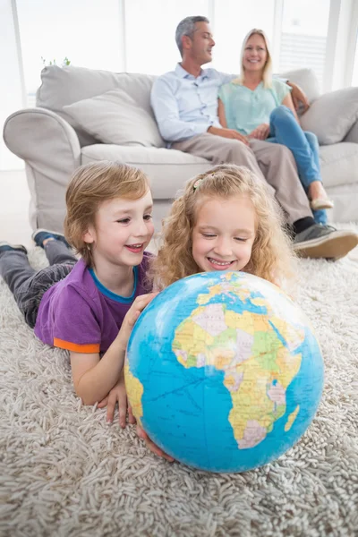 Children exploring globe while parents sitting on sofa — Stock Photo, Image